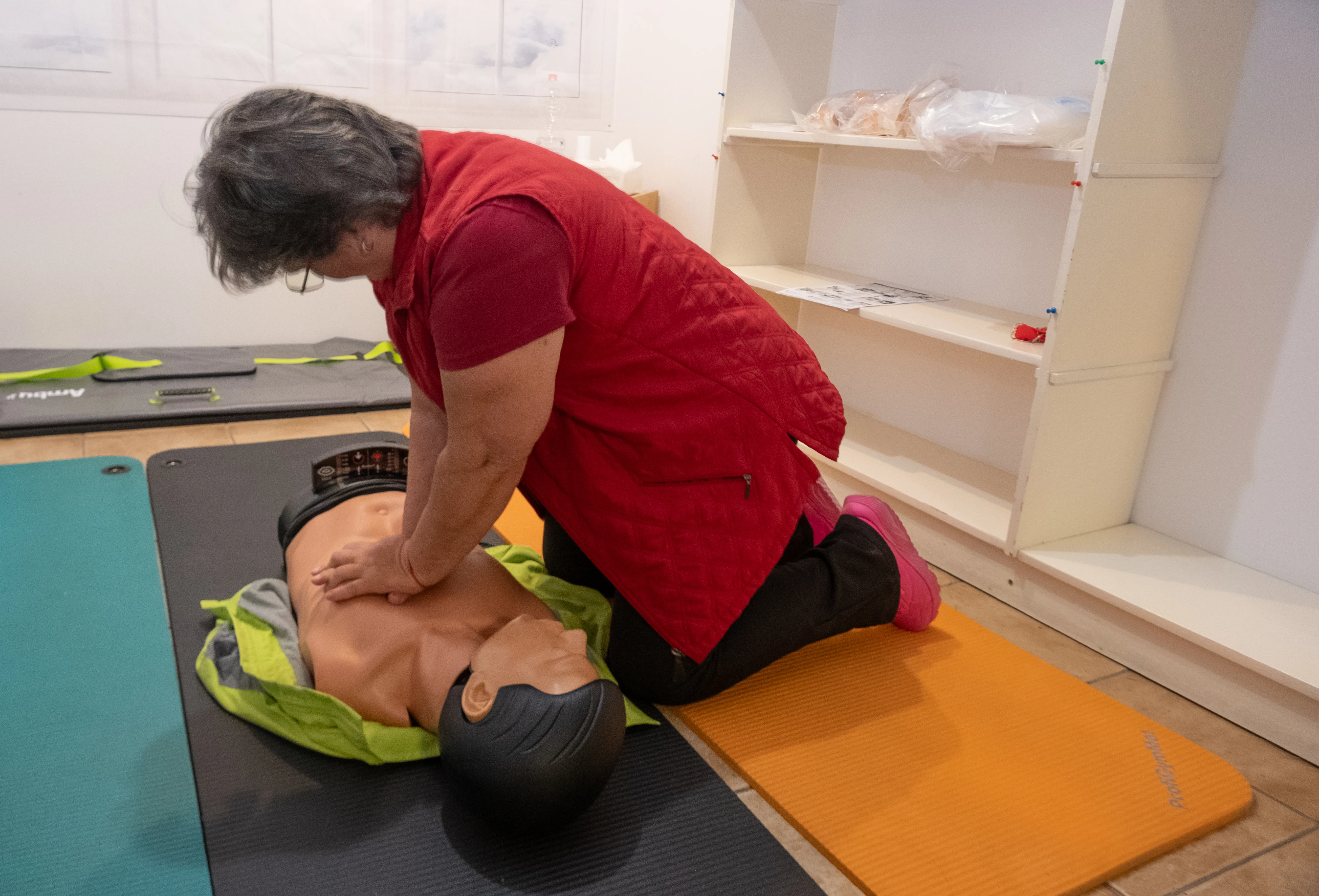 A szőnyegen egy ambubaba, mellette térdel egy piros felsős hölgy, aki az újraélesztésen tanultakat gyakorolja